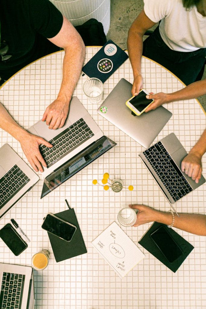 Top view of a team collaborating with laptops, phones, and notes in a modern office.